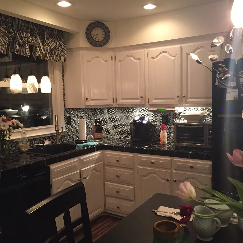 Churchville kitchen before renovation with dated white raised-panel cabinets, black tile countertops, a dark mosaic backsplash, and black appliances